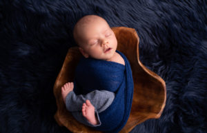 This is a newborn photography image of Baby wrapped and placed in wooden bowl