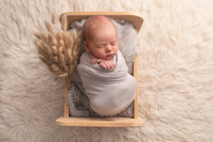 This is a newborn photography image of newborn baby in wooden bed and white flokati