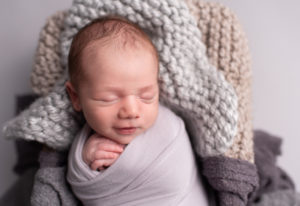 Newborn baby boy smiling on grey blanket