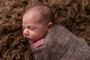 Profile shot with newborn wrapped in a brown wrap and brown flokati