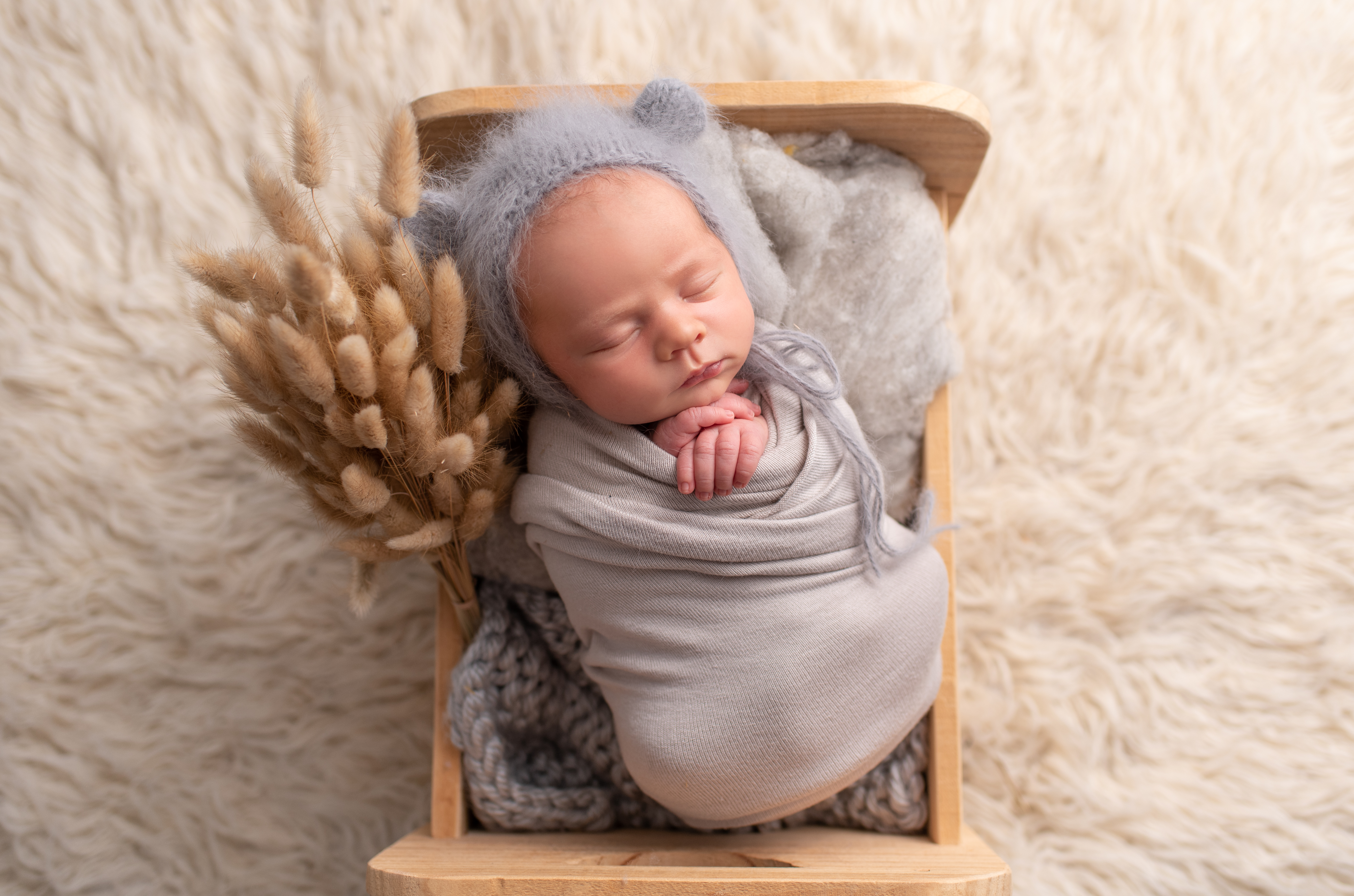 This is a newborn photography image of a newborn baby in wooden bed and bear hat