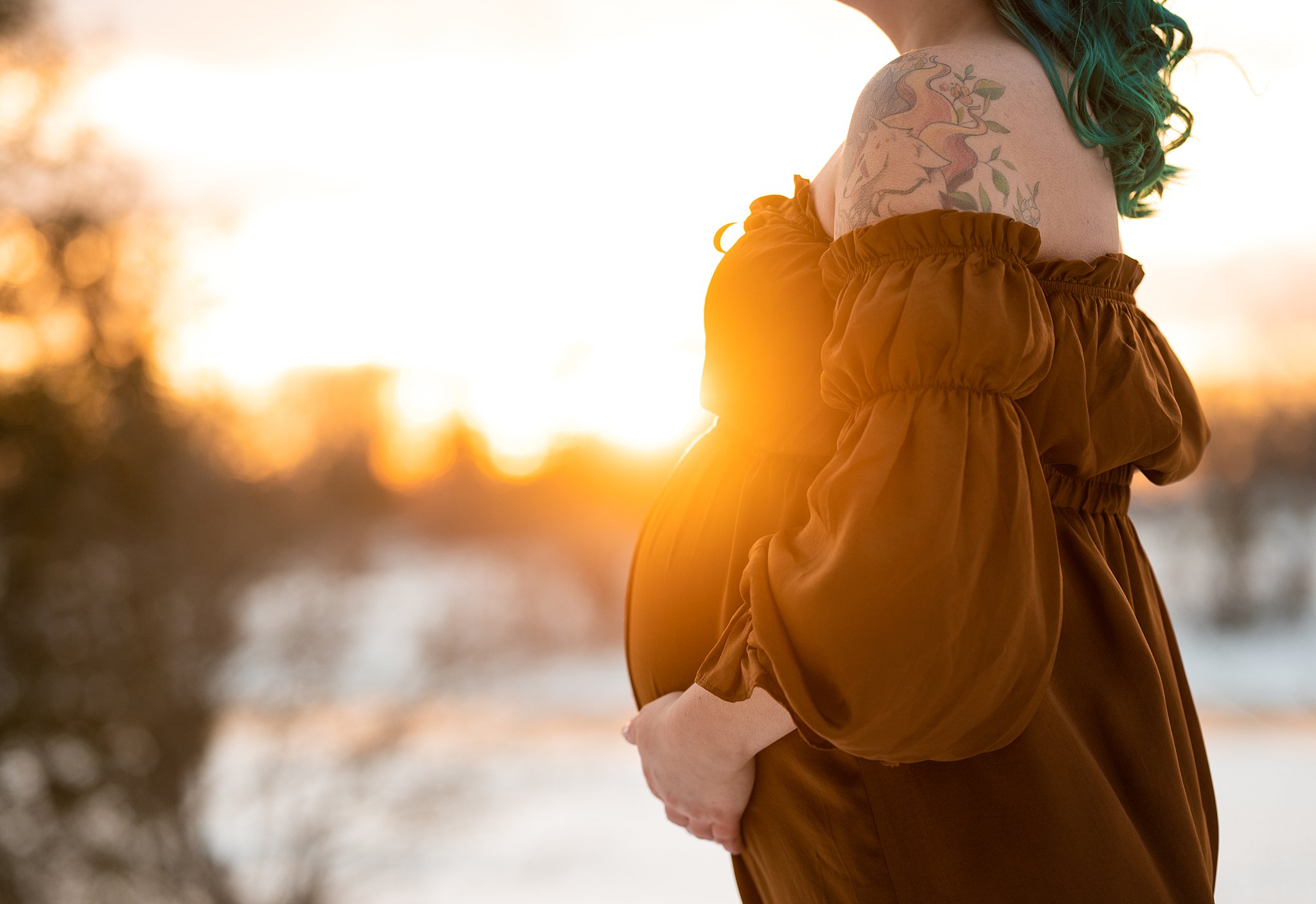 mother to be in a brrown maternity dress stands outside with the setting sun behind her Ottawa Birthing Centre