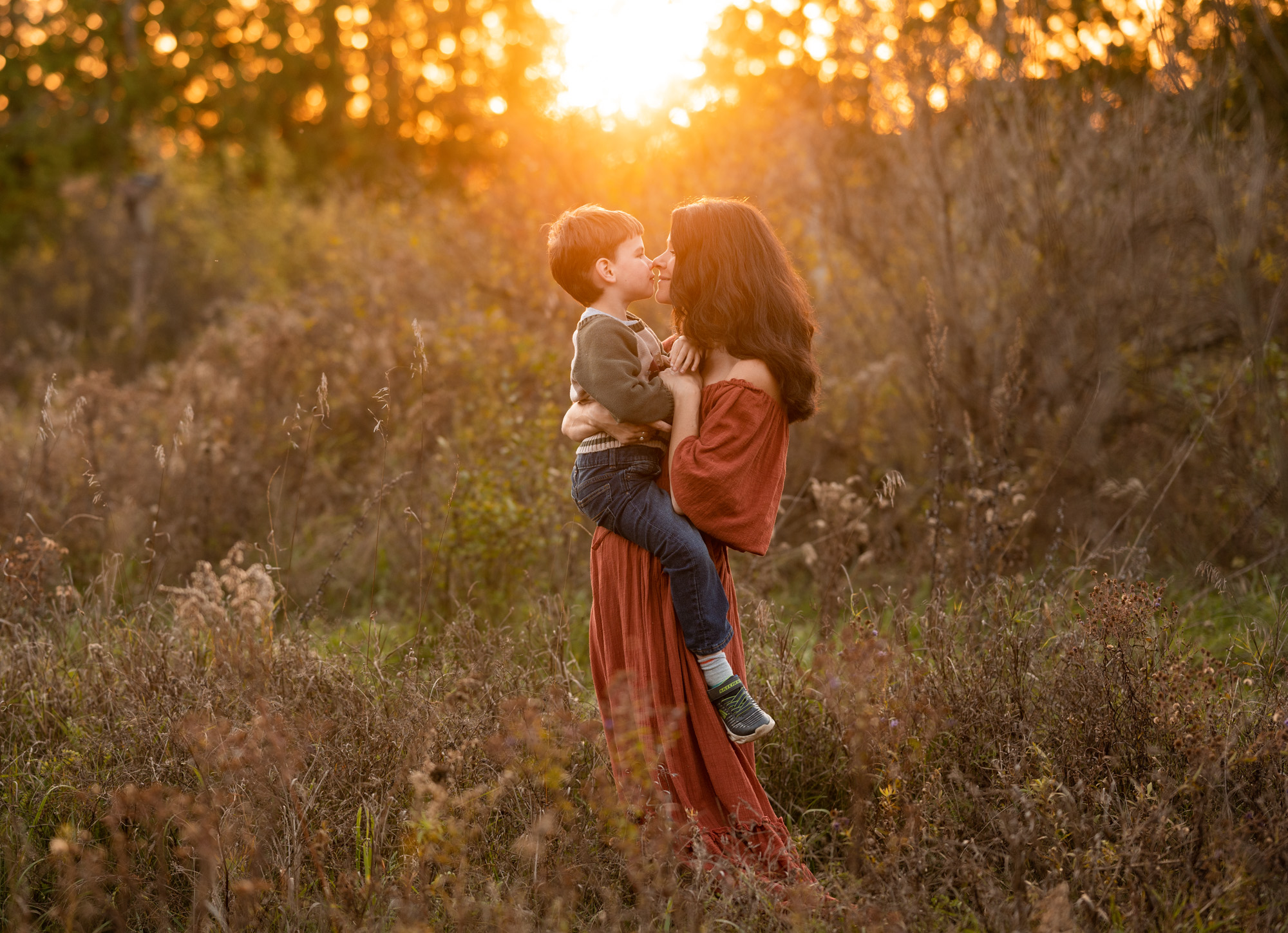 mom to be in rust gown holding her son in a field