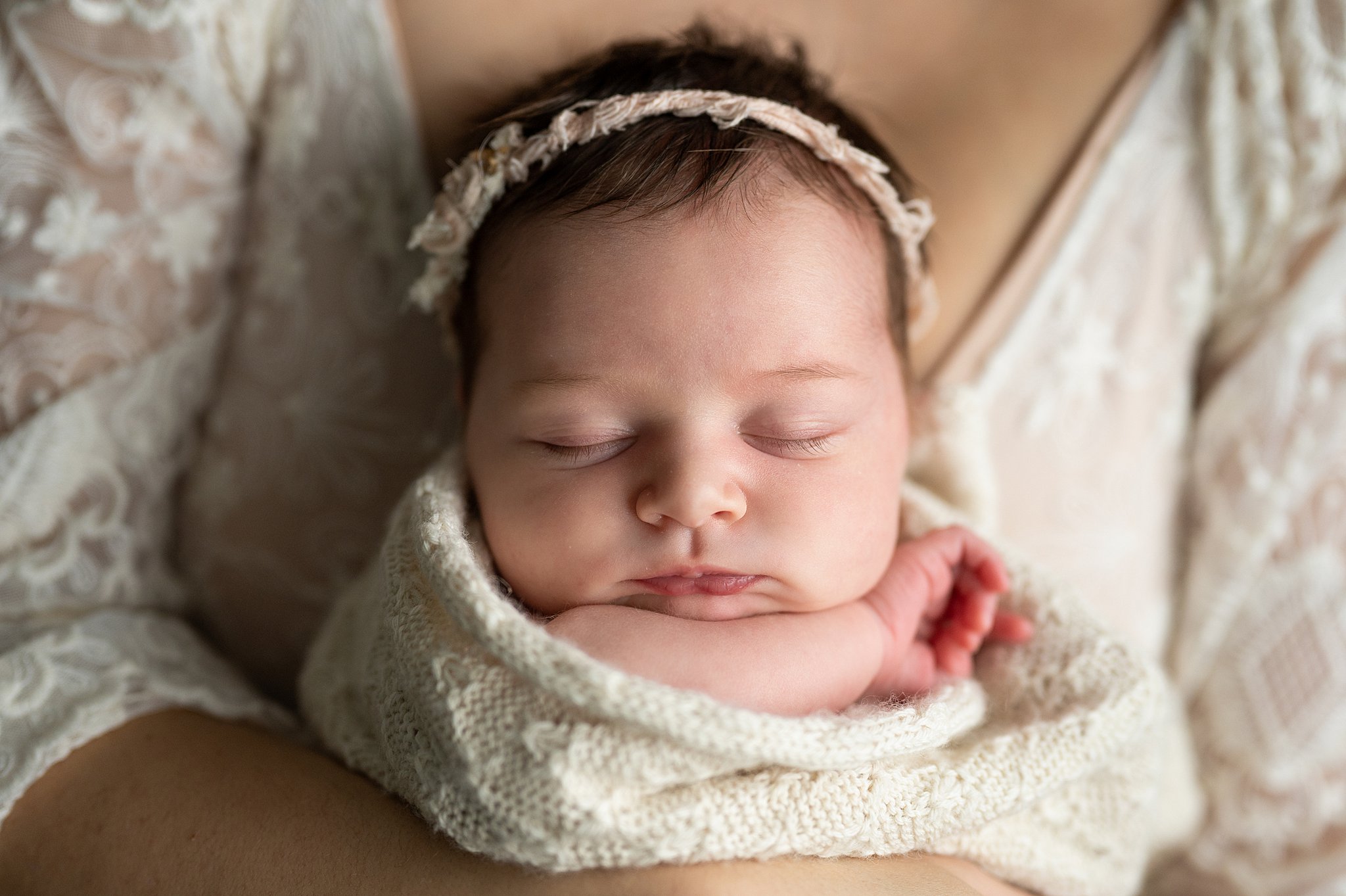 sleeping newborn with a headband sleeps in mother's arms