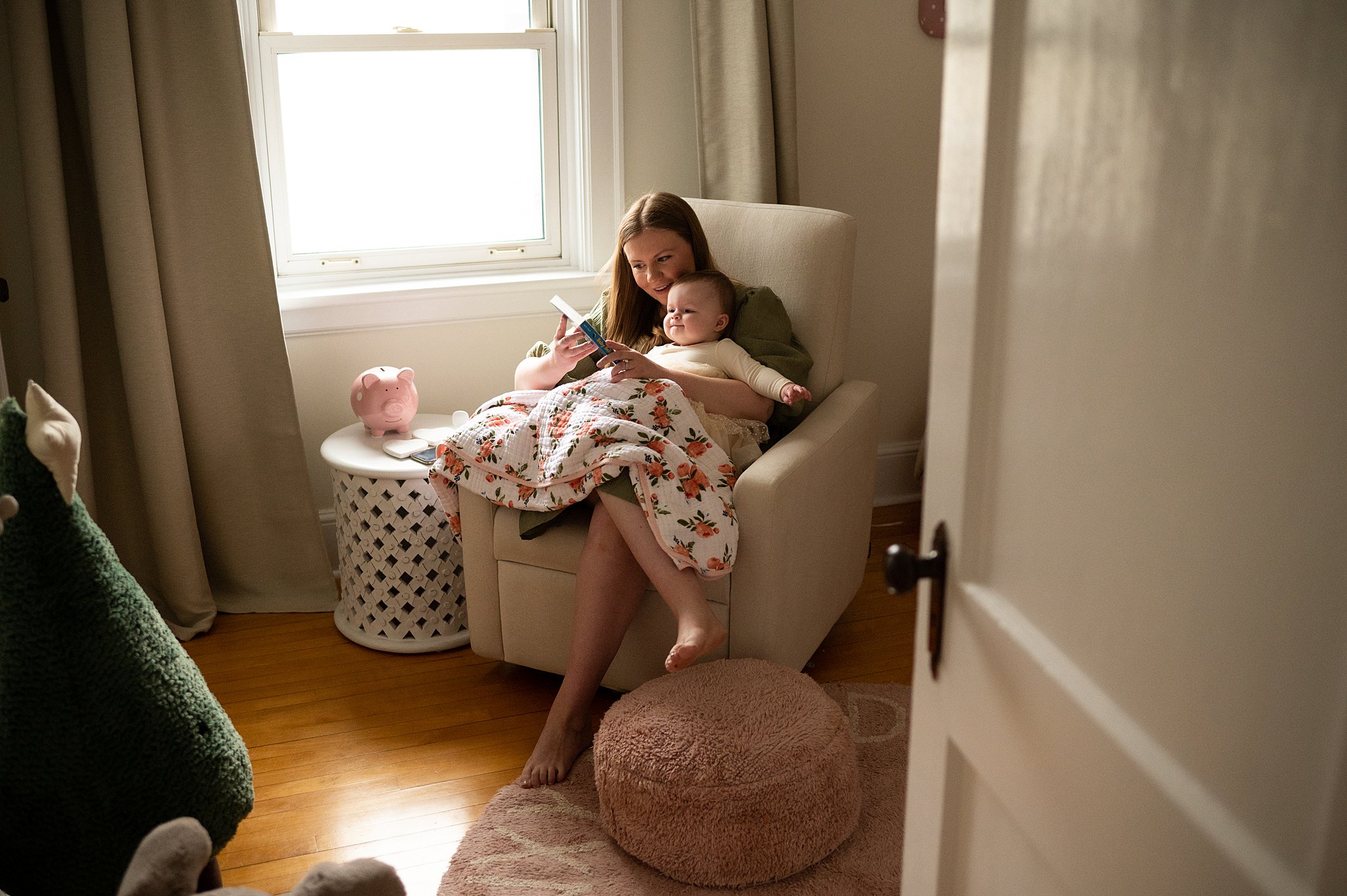Mother sits in a nursery chair by a window reading to her toddler in her lap with a floral blanket over them baby enroute ottawa