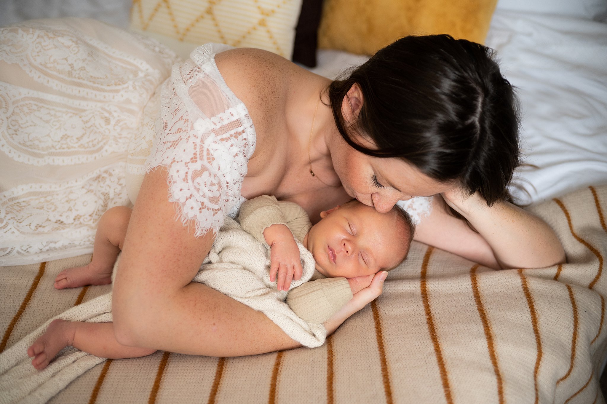 mother in a lace dress cuddles her newborn on a bed