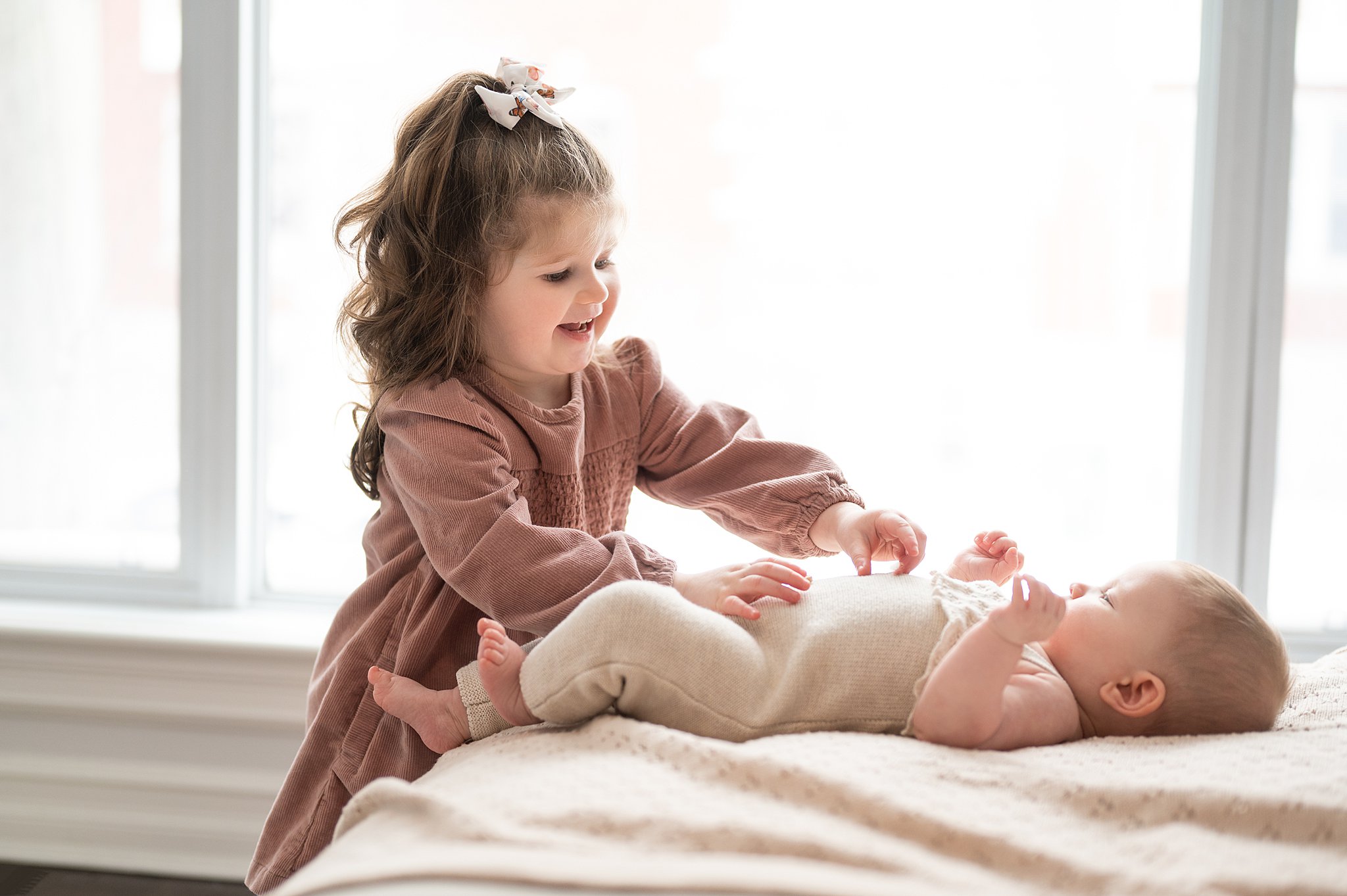 little girl playing with her newborn baby sibling on a bed