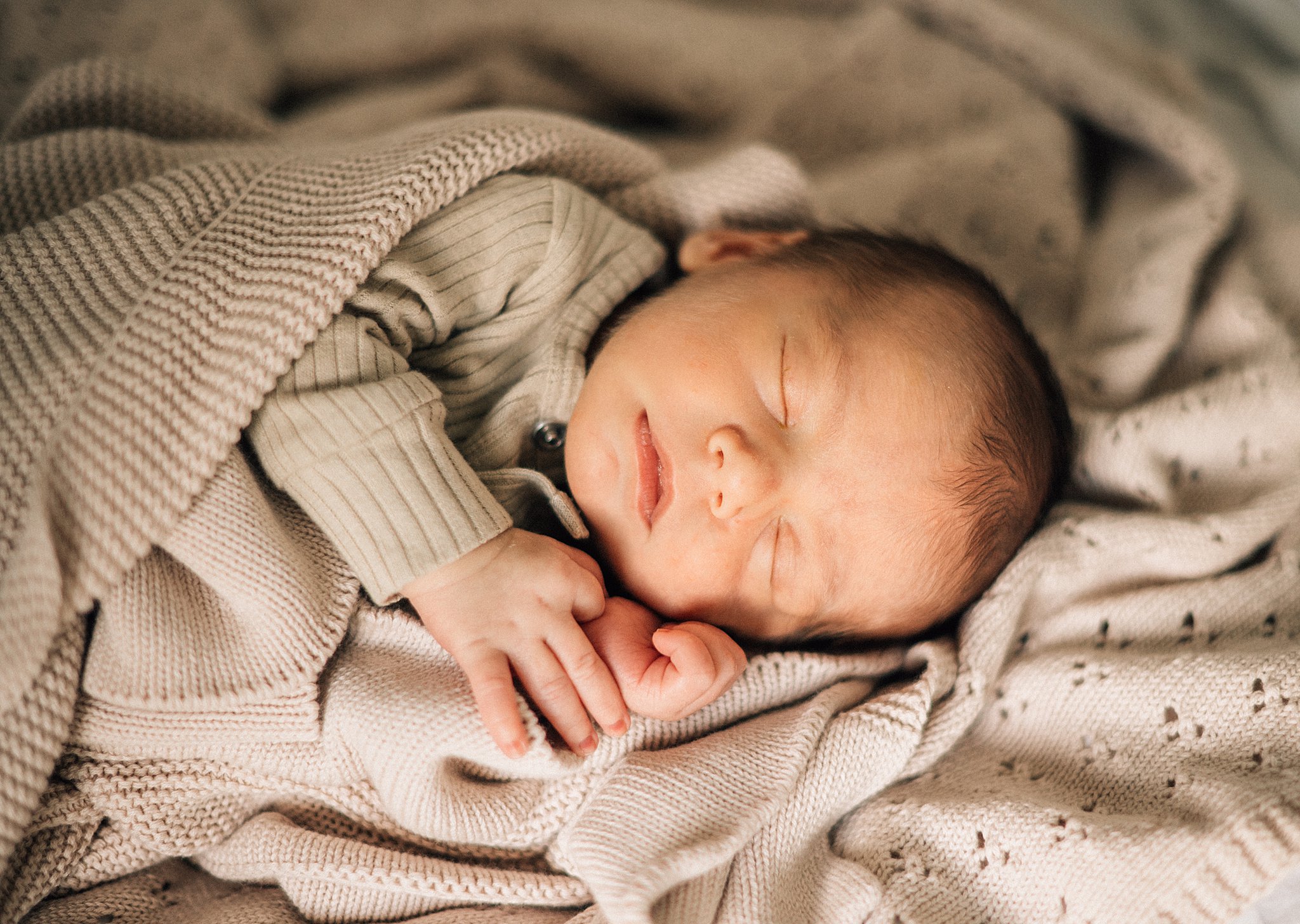 A newborn baby sleeps on its side in a tan onesie among matching knit blankets ottawa prenatal yoga