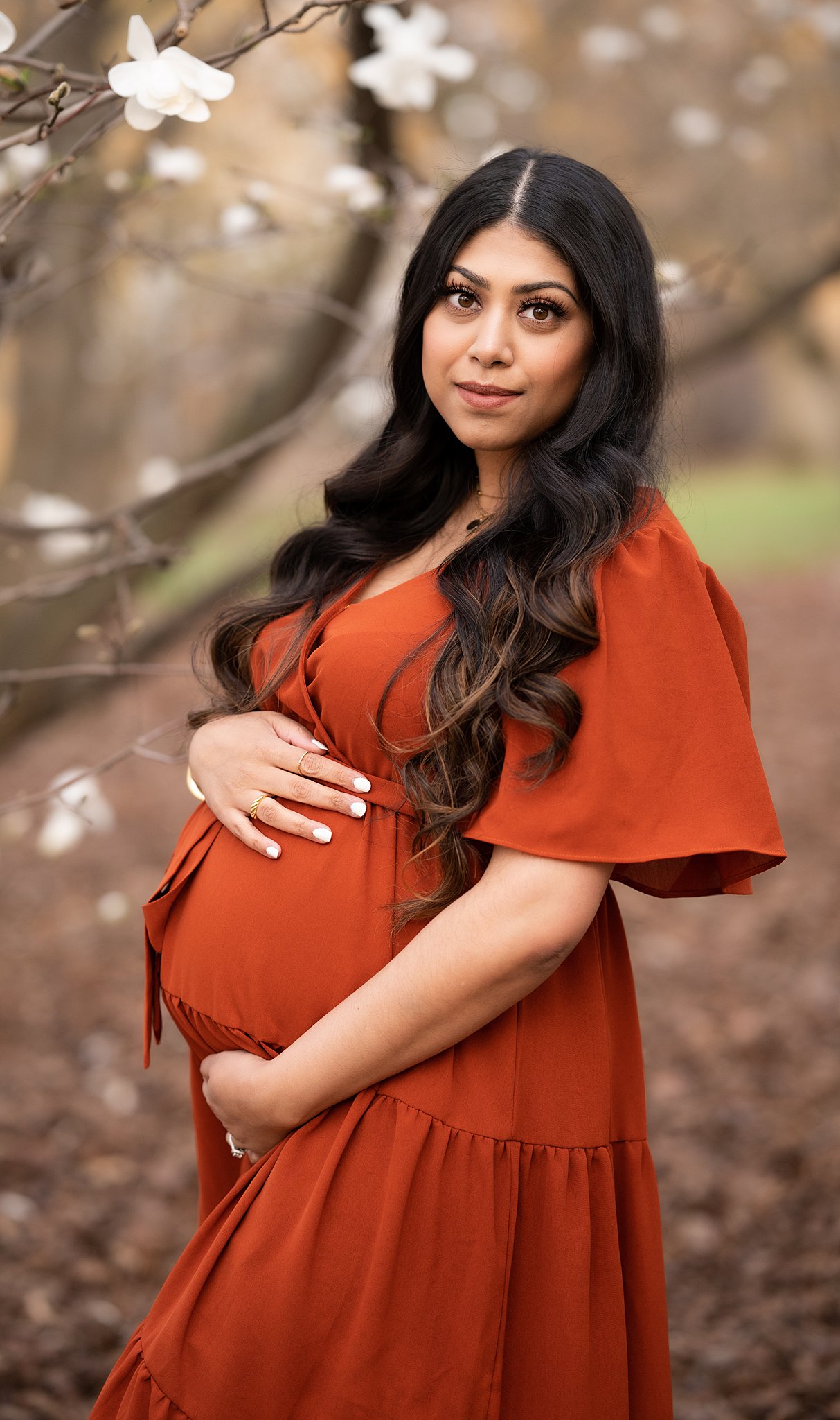 A mom to be holds her bump while standing in a park
